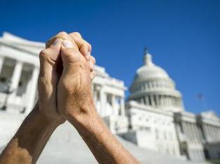 Two hands clasped together in front of a state capital building.